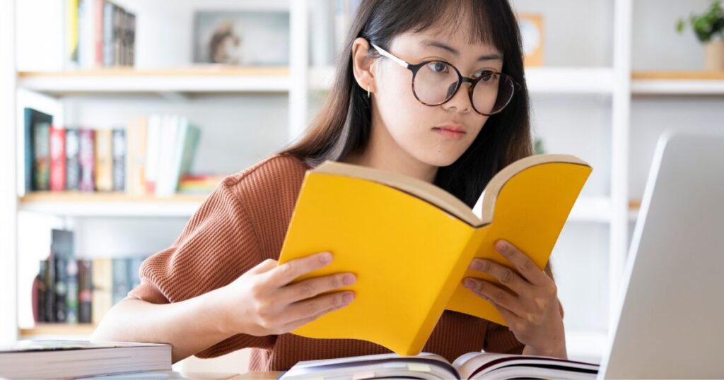 本とパソコンを見て学んでいる女性